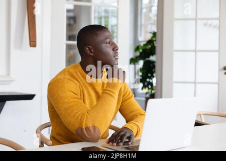 Thoughtful african american man using laptop at home and looking away Stock Photo