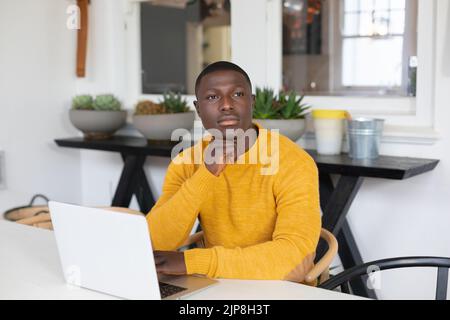 Thoughtful african american man using laptop at home and looking away Stock Photo