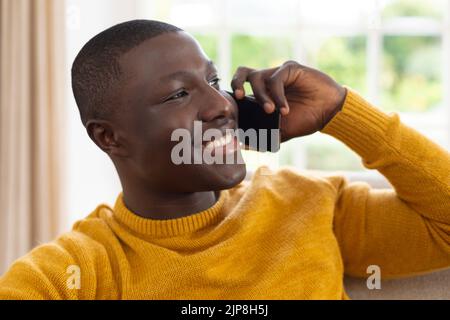 Smiling african american man sitting on couch talking on smartphone Stock Photo