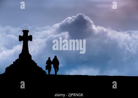 The silhouette of a couple walking past the large War Memorial Cross in Newquay in Cornwall in the UK. Stock Photo