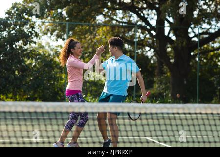 Smiling biracial couple playing tennis shaking hands on outdoor tennis court Stock Photo