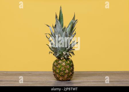 Pineapple on a wooden table with a yellow background, whole. Stock Photo