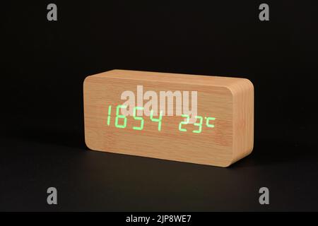Electronic digital wooden clock with thermometer on a black background close-up. Stock Photo
