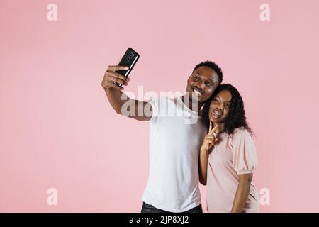 Joyful people using mobile phone to take selfies together in studio. Man and woman taking picture with smartphone and having fun in front of camera. Carefree couple feeling happy. Stock Photo