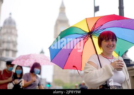 A tourist shelters beneath an umbrella near to the Houses of Parliament in Westminster, central London. Yellow weather warnings are in place for most of the UK on Tuesday after weeks of little rain and warm conditions have caused droughts, leaving land parched. Picture date: Tuesday August 16, 2022. Stock Photo