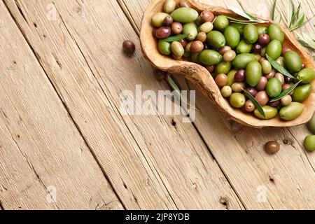 Mixed olives in wooden dish on planks background Stock Photo