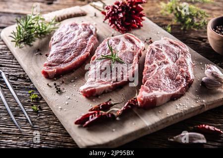 Three sliced pieces of pork neck with herbs, chili spices and garlic on a cutting board. Stock Photo