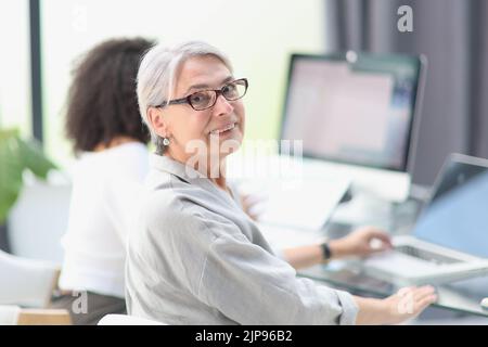 Smiling 60-year-old business woman using a computer at office Stock Photo