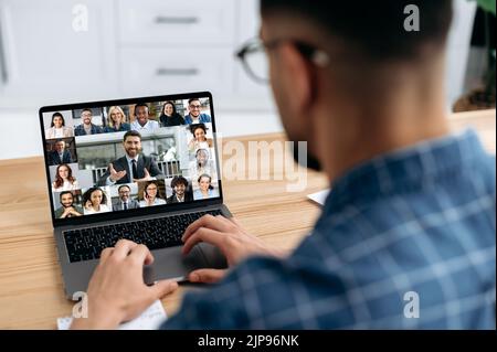 Over shoulder view at a laptop screen with different people, employees, business partners, male conducts online briefing, brainstorming, group conversation. Online video communication concept Stock Photo