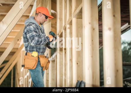Caucasian Middle Aged Construction Worker Wearing Leather Tool Belt Holding Electric Screwdriver in His Hands Ready to Start Working on Wooden Skeleto Stock Photo