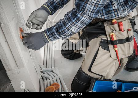 Professional Electrician in Protective Gloves and Tool Belt Working on Installing Power Sockets in the Wall. Plastic Pipeline in the Background. Indus Stock Photo