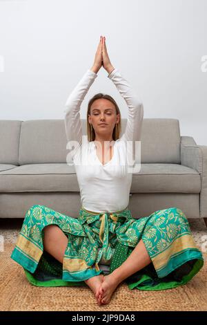 young blonde woman meditating in the living room at home Stock Photo