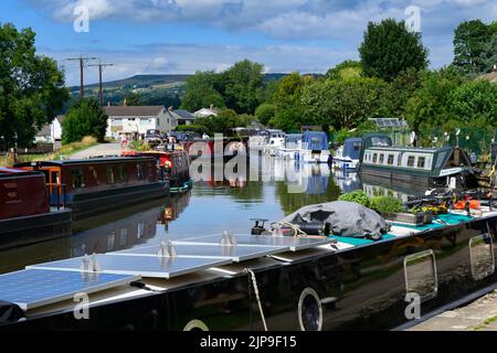 Barges at busy moorings, self-drive hire boat traveling, scenic sunny stretch of Leeds Liverpool Canal & towpath - Bingley, West Yorkshire England UK. Stock Photo