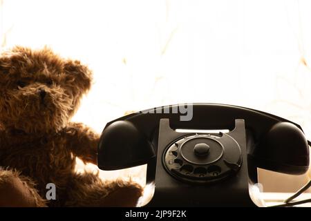 Children's teddy bear sits near the old telephone at home and is sad, retro phone Stock Photo