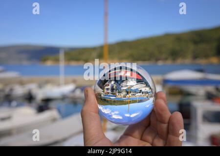 Hand holding glass sphere in the small harbor of Valun (Cres, Croatia), sunny day in springtime Stock Photo