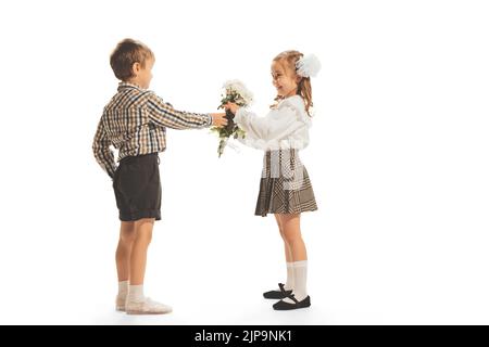 Portrait of children, boy giving girl flowers isolated over white studio background. Retro fashion Stock Photo