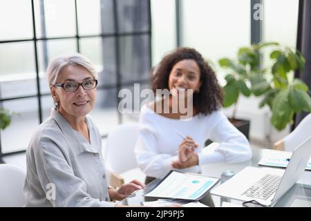 Two business women smile while working together on a laptop at a table in the boardroom in the office Stock Photo