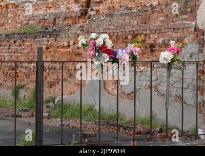 Memorial flowers on a iron fence with a wooden cross.  Old brick wall background. Stock Photo