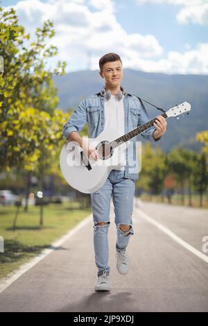 Young man playing an acoustic guitar and walking outdoors on a pedestrian lane in a city Stock Photo