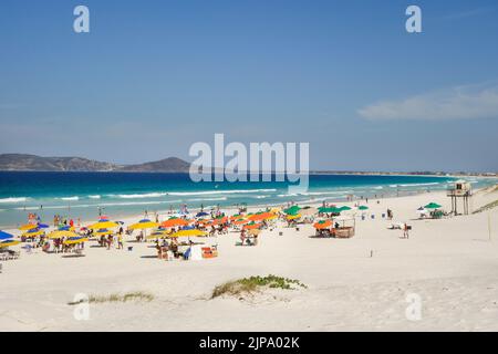 colorful umbrellas and tourists crowd the sand line at Praia do Forte in Cabo Frio, Rio de Janeiro, Brazil. Stock Photo