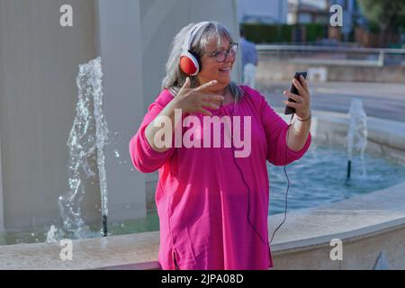 woman with white hair and glasses making a video call with her cell phone smiling Stock Photo