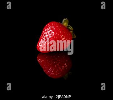 Single ripe red strawberry on a black reflective background Stock Photo