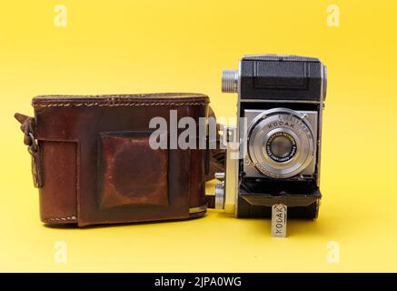 A vintage Camera from Kodak with old protective leather case isolated on a yellow background Stock Photo