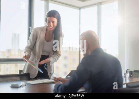 Colleagues having business meeting in the boardroom. Businesswoman standing at office desk and presenting strategy. Stock Photo