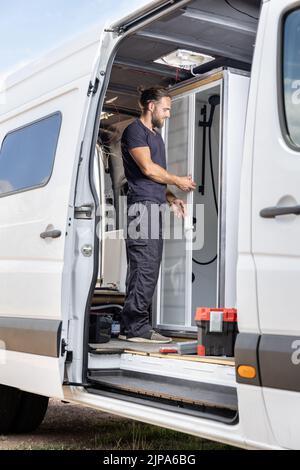 Man working on a shower room inside a camper van Stock Photo