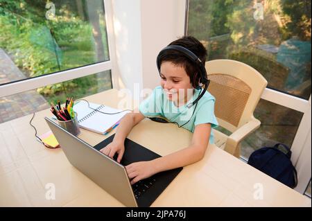 Top view of school child studying in an online school, sitting at laptop and typing text , watching a video lesson. Stock Photo