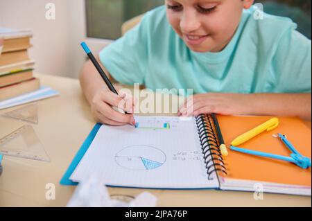 Student's hand holds a pencil, paints the perimeter of a rectangle drawn in notebook, doing homework on geometry at home Stock Photo