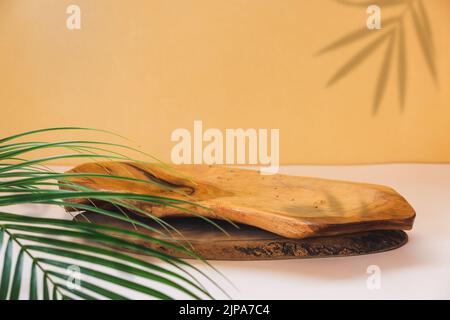 Rustic wood plate  podium. Background for  product presentation, palm leaf and natural shadow on the wall. Selective focus, copy space Stock Photo