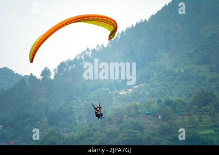 para gliding people with a bright orange yellow glider in the middle of hills mountains near nanital bir billing showing a popular adventure sport for Stock Photo