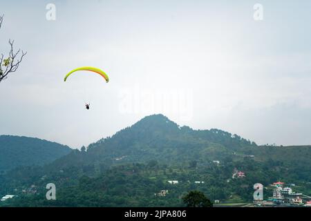 para gliding people with a bright orange yellow glider in the middle of hills mountains near nanital bir billing showing a popular adventure sport for Stock Photo