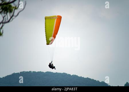 para gliding people with a bright orange yellow glider in the middle of hills mountains near nanital bir billing showing a popular adventure sport for Stock Photo