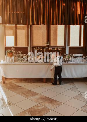 Boy stand eating near catering wedding buffet for events. Beautifully decorated catering banquet table food snacks and appetizers with sandwich Stock Photo