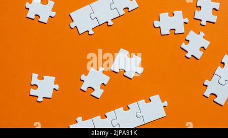 White puzzle pieces on the orange background. Concept of board game. Stock Photo