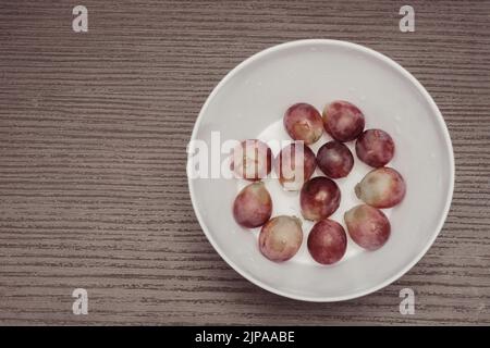 plate with a serving of fresh red globe grapes, a healthy snack for pre-workout meals. Natural low-fat diet with antioxidants and polyphenols Stock Photo