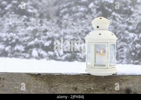 An iron lantern with candle on the wooden fence in the garden. Winter. time Stock Photo