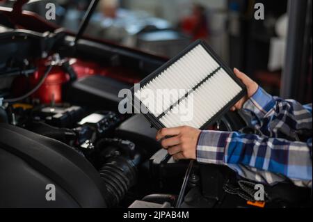 Caucasian female auto mechanic changes the engine air filter in the car. Stock Photo