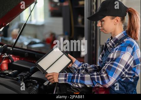 Caucasian female auto mechanic changes the engine air filter in the car. Stock Photo
