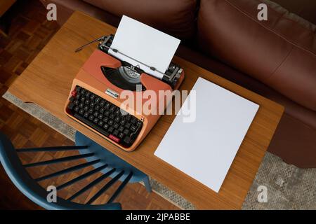 Photograph from above of a 1970's Underwood 20 typewriter on a teak desk, a sheet of paper in the typewriter and a stack of blank paper to the side. Stock Photo