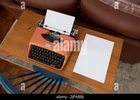 Photograph from above of a 1970's Underwood 20 typewriter on a teak desk, a sheet of paper in the typewriter and a stack of blank paper to the side. Stock Photo