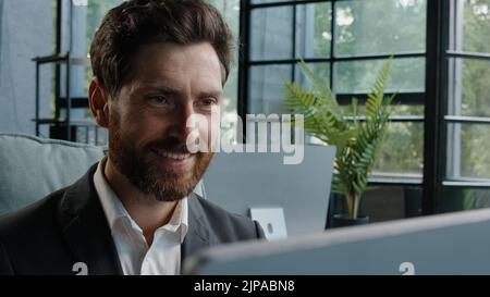 Close-up male worker leader Caucasian businessman bearded mature adult 40s manager looking at window smiling working with computer think about idea Stock Photo