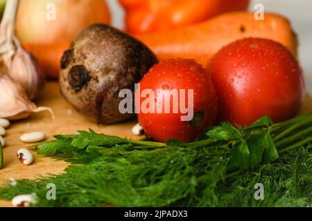 Close-up of tomatoes with various vegetables for cooking borscht on a wooden board in the kitchen. Stock Photo