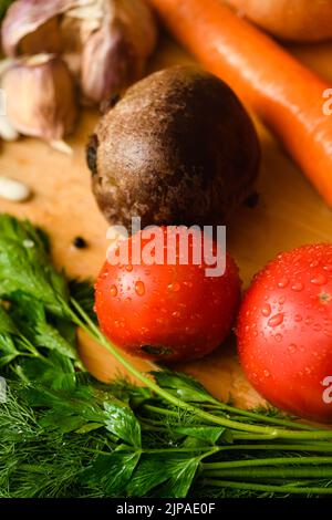 Close-up of tomatoes with various vegetables for cooking borscht on a wooden board in the kitchen. Top view. Stock Photo