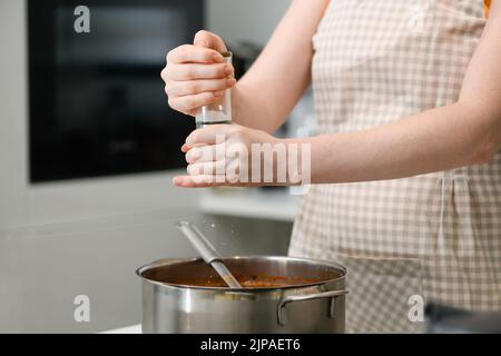 A woman cooks Ukrainian borscht in the kitchen. A woman in an apron adds spices to borscht. Stock Photo