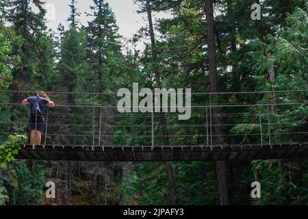 Hiker crossing a suspension bridge over a river, forest background. Canada, Btitish Columbia Stock Photo