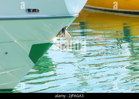 Chrome-plated metal anchor on the bow of the boat in the bay Stock Photo