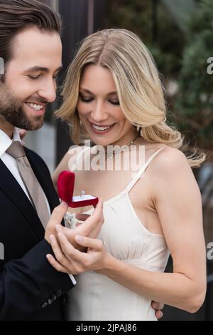 Smiling man in suit holding box with engagement ring near girlfriend outdoors Stock Photo